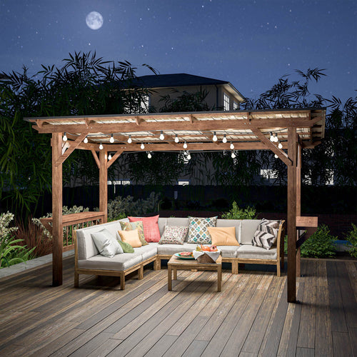 The pergola lit at night over a deck with a sectional sofa beneath it