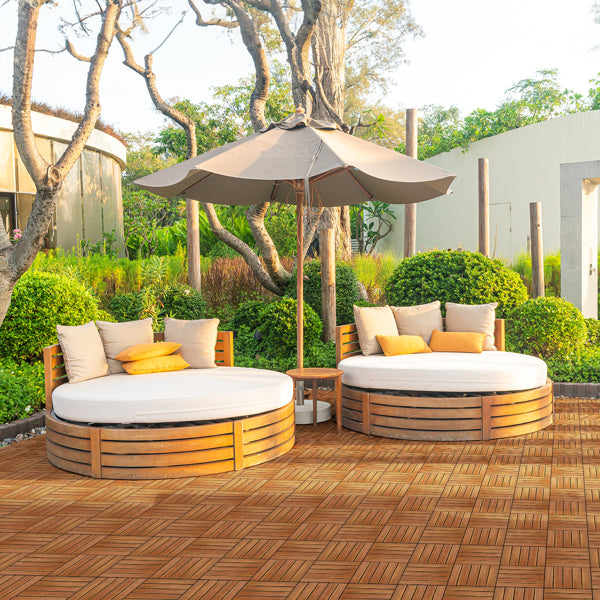 Two round wooden daybeds with cushions and a parasol standing on a tiled garden terrace