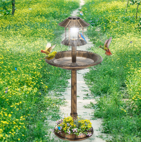 The bird bath standing beside a grass path through a meadow of yellow wildflowers, its solar lamp lit and hummingbirds hovering at the basin