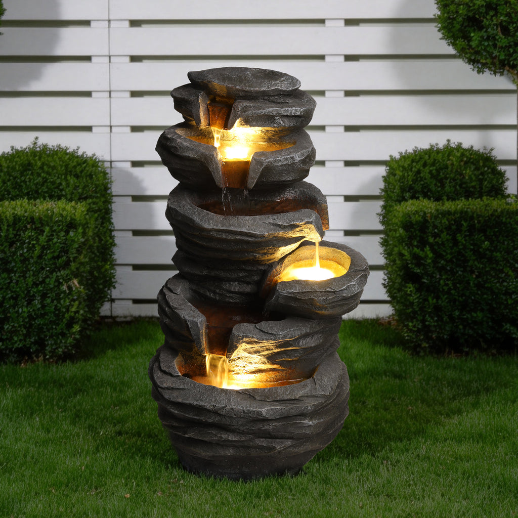 Stacked rock fountain on a lawn beside a hedge