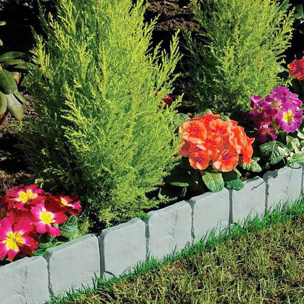 The edging separating a grass lawn from a planting bed of conifers, orange and pink blooms