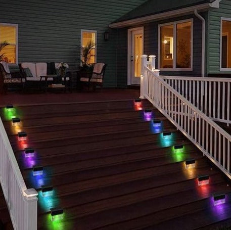 A row of the lights along a deck stair rail, cycling through colors at night