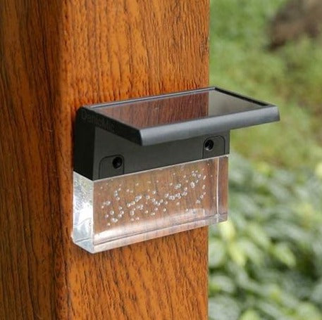 Solar fence light mounted on a wooden post, glass lens lit at dusk